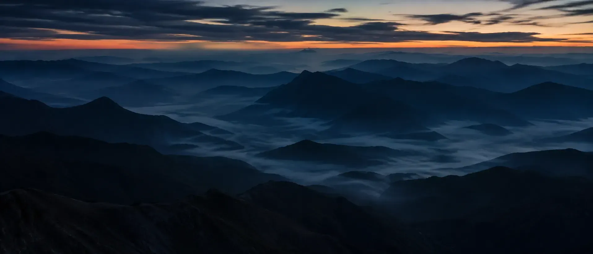 Layered mountain ridges receding into dusk haze above a valley of fog